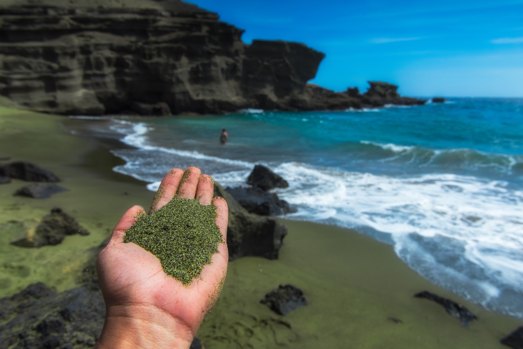 Green olivine sand held over a naturally green beach